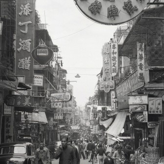 Rotund Hong Kong Vremurile Vechi, Imagine în alb-negru cu o stradă aglomerată din Hong Kong, cu magazine tradiționale.