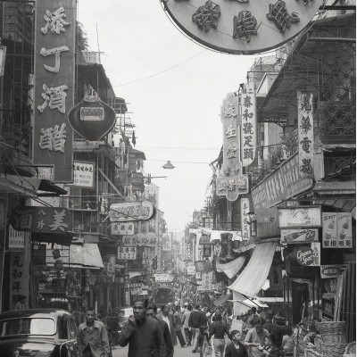 Rotund Hong Kong Vremurile Vechi, Imagine în alb-negru cu o stradă aglomerată din Hong Kong, cu magazine tradiționale.